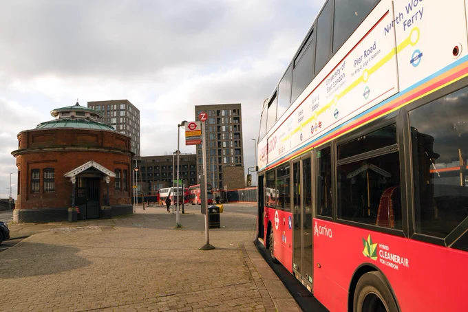 A superloop bus next to the north entrance of the Woolwich foot tunnel. Blocks of flats in the distance.