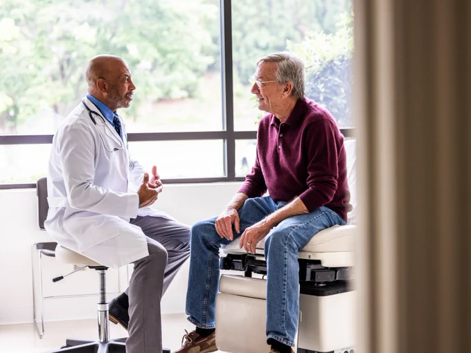 Male doctor talking with a senior man in an exam room.