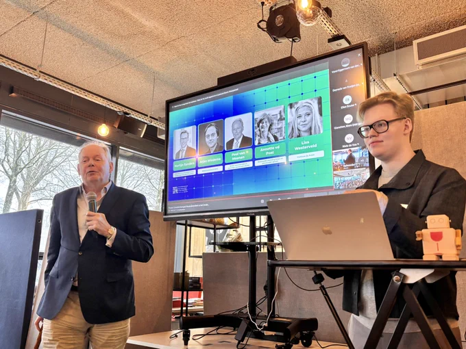 Foto van Paul van Meenen (senator D66) en Elijah Delsink (LBVSO) in een zaak vanaf de eerste rij. Paul staat links en heeft een microfoon in zijn handen. Elijah rechts achter een laptop. Achter hen een scherm met daarop foto’s van mensen die vandaag een praatte houden.