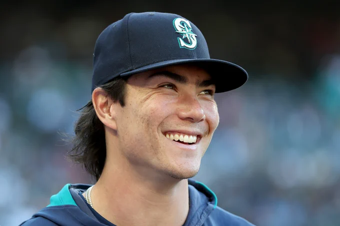 Candid picture of Bryan Woo smiling. He wears a blue Mariners hoodie and cap.