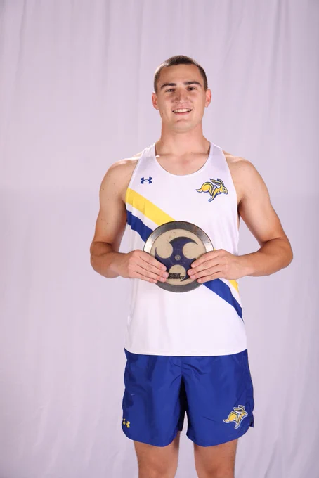 A tall track and field athlete poses with a discus