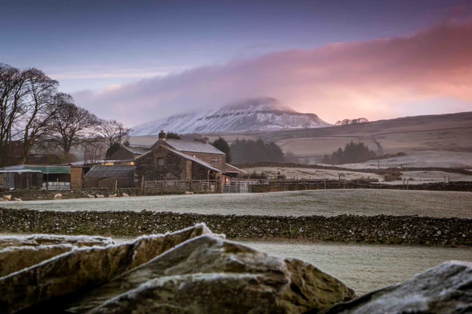 Stone farmhouse and outbuildings set in frosty fields with a misty mountain backdrop of Pen-y-Ghent at sunrise.