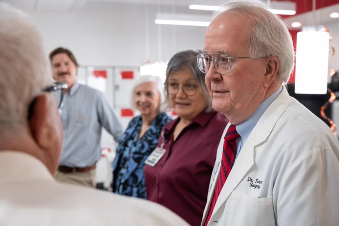 A group of professionals, including Dr. Tom Gregg, engaging in a conversation in a modern office setting.