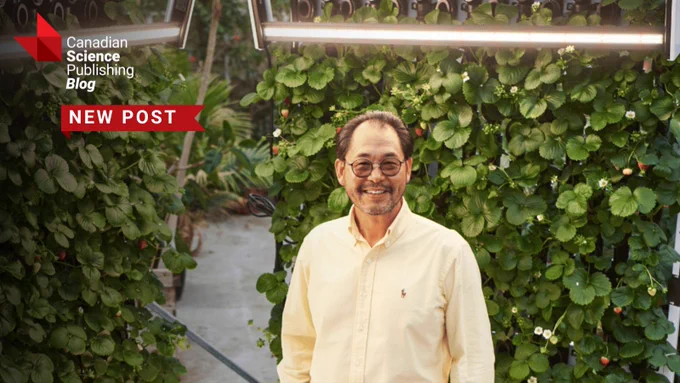 Man in a light yellow shirt standing inside a greenhouse surrounded by lush green plants with white flowers promoting the new Canadian Science Publishing Blog post.