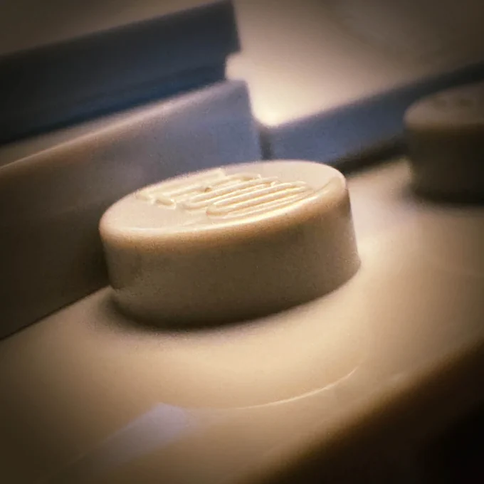 A very close-up photograph of a single stud on a grey, modular building block set. It is extremely mysterious. *twirls moustache*