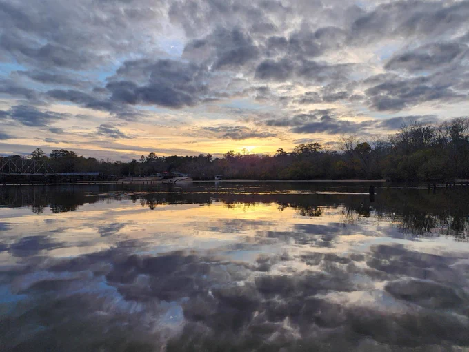 Calm river reflecting a dramatic cloudy sky at sunset with trees lining the horizon.