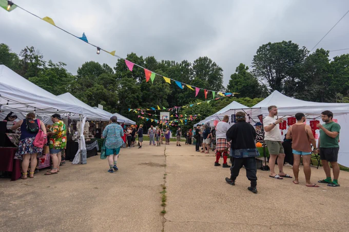 The artist alley at MAGStock under tents and decorative flags. Attendees gather as vendors purvey their wares at each booth.