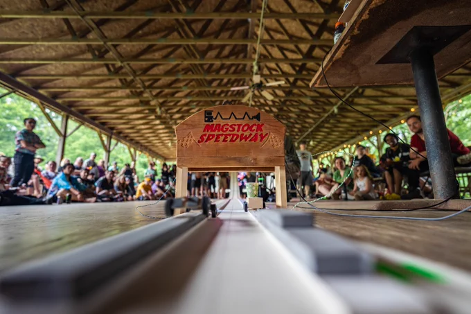 The MAGStock pinecar derby, taken from an angle behind the finish line. A race is currently underway with attendees and competitors looking on from the distance.