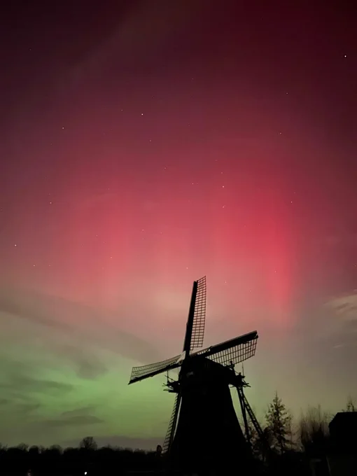 Photo of green and red aurora over a windmill