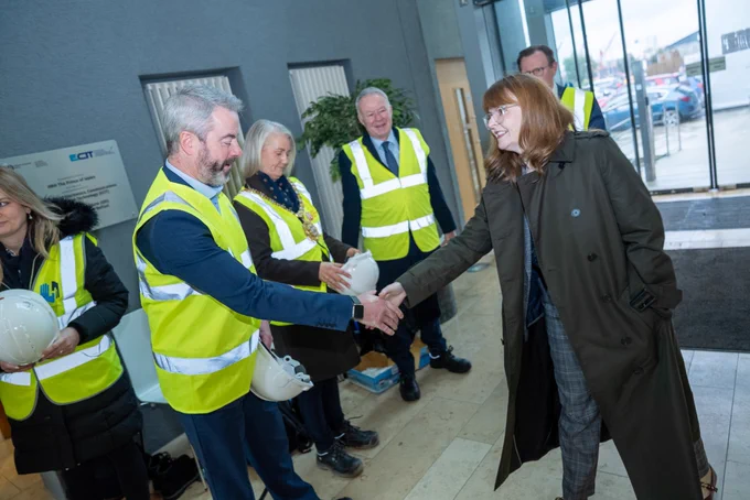 Image shows Economy Minister, Dr Caoimhe Archibald, shaking hands with a member of Queen's staff, with four other people in the background.