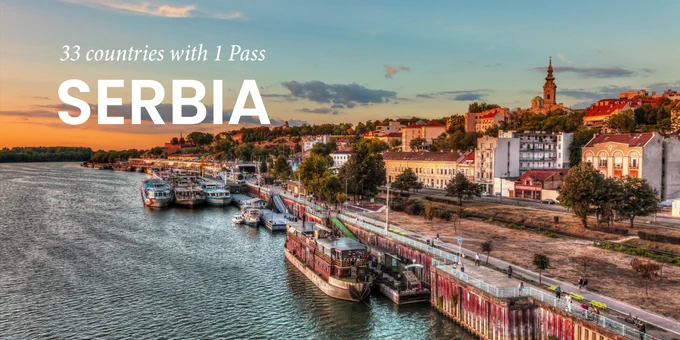 Promotional image featuring a serene sunset view of the riverfront in Serbia with multiple boats docked along the shore. The image includes text promoting travel across 33 countries with 1 Pass.

