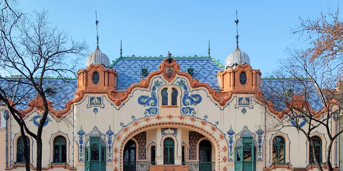 Facade of the ornate Gellért Baths in Budapest, featuring Art Nouveau architecture with elaborate ceramic decorations and tiled roof.
