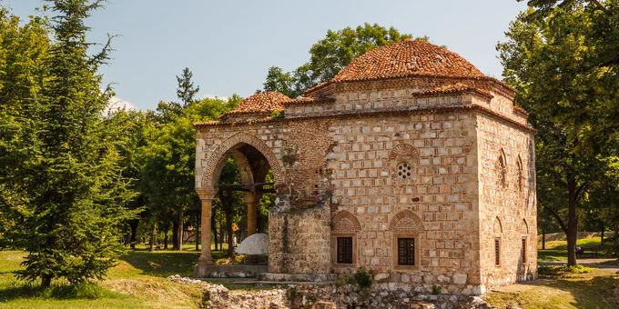 View of the historic Bali Beg Mosque in Niš, Serbia surrounded by green trees under a clear sky.
