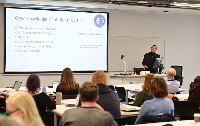 A slide presentation on 'open knowledge institutions' to an attentive classroom audience in a modern lecture hall.