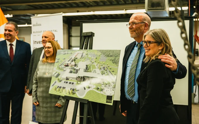Four people in business attire stand and smile beside an easel displaying an architectural rendering of a hospital building during an indoor event or announcement.
--
Quatre personnes en tenue de travail se tiennent debout et sourient à côté d'un chevalet affichant un rendu architectural d'un bâtiment hospitalier lors d'un événement ou d'une annonce en intérieur.