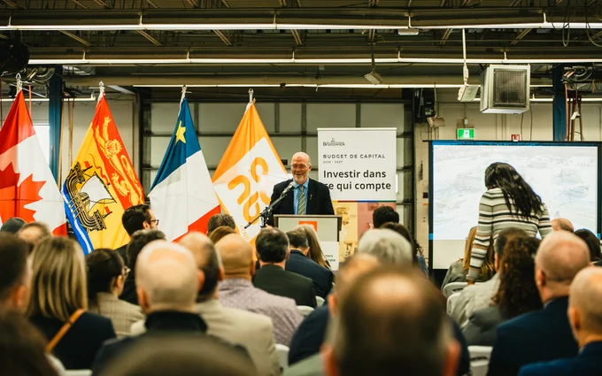 A man speaks at a podium to an audience in a large room, with five flags behind him, including the Canadian flag. A sign reads "Investir dans ce qui compte." People are seated and facing the speaker.
--
Un homme s'adresse à un public dans une grande salle, avec cinq drapeaux derrière lui, dont le drapeau canadien. Un panneau indique "Investir dans ce qui compte". Les personnes sont assises et font face à l'orateur.