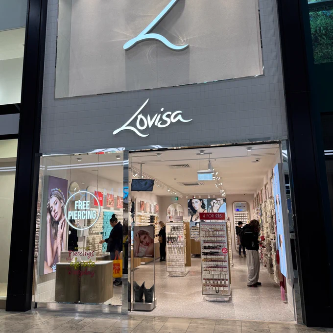 Front view of a Lovisa store, featuring large promotional posters, a display of jewelry on racks, and customers browsing inside.