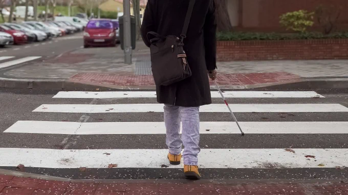 A person with a white cane crosses a street 