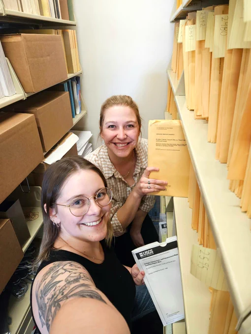 Photo of two Astrogeology mappers with historical maps (in yellow folio) and newer maps (in white folio) that are available for visitors to take home from a visit to Astrogeology.
