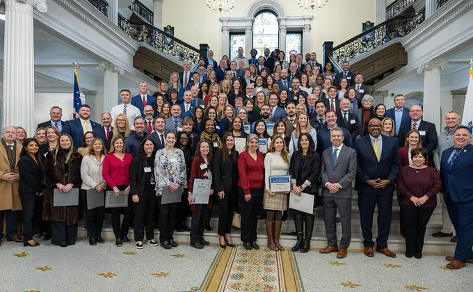 Dozens of people gather around and on the Grand Staircase at the State House with Massachusetts education officials.