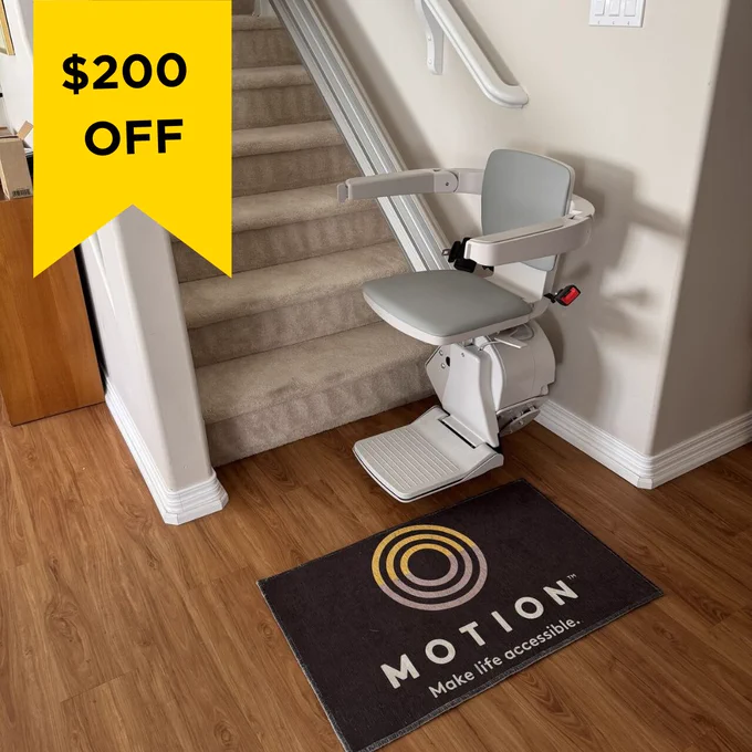 Grey stairlift installed on carpeted stairs with a $200 off yellow banner in the top left corner. A Motion-branded floor mat is also pictured with the stairlift. 