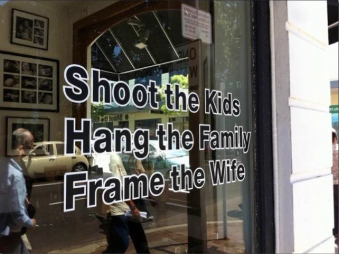 Text on the window of a shop that frames photos: "Shoot the Kids / Hang the Family / Frame the Wife"