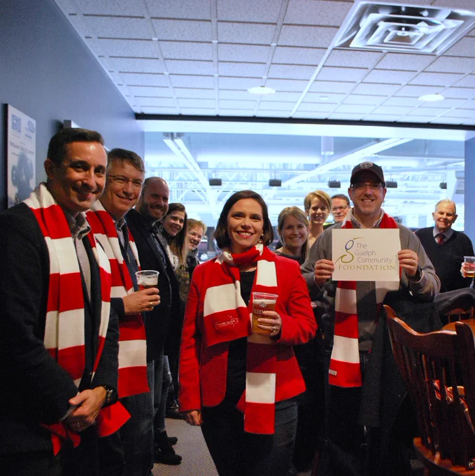 People standing together in the boxseats at the hockey arena with red and white scarves holding the GCF sign