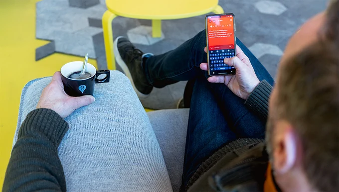 A man sitting in on a couch, holding a phone with de slimste mens app