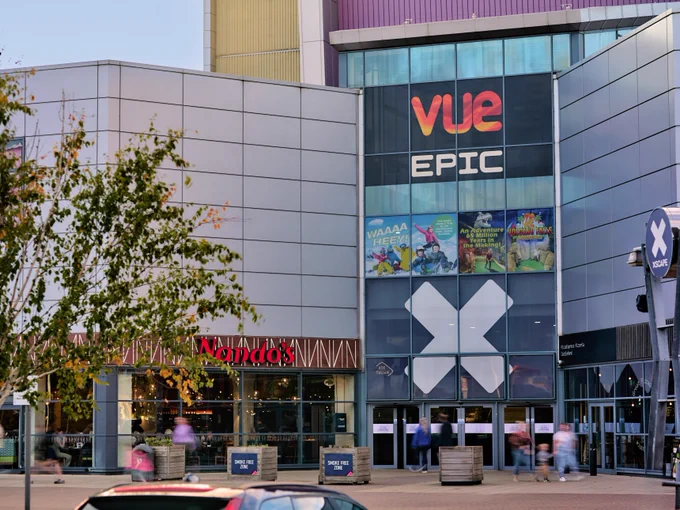 Exterior view of a modern building featuring signs for Vue Cinema and Nando's restaurant, with a large "X" logo displayed prominently.