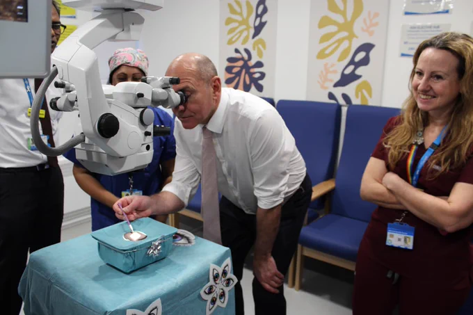 Sir Jim Mackey is seen looking down a surgical microscope to observe dummy cataract surgery.