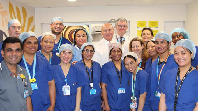 Staff are pictured with Sir Jim Mackey. The staff are wearing blue hospital scrubs.