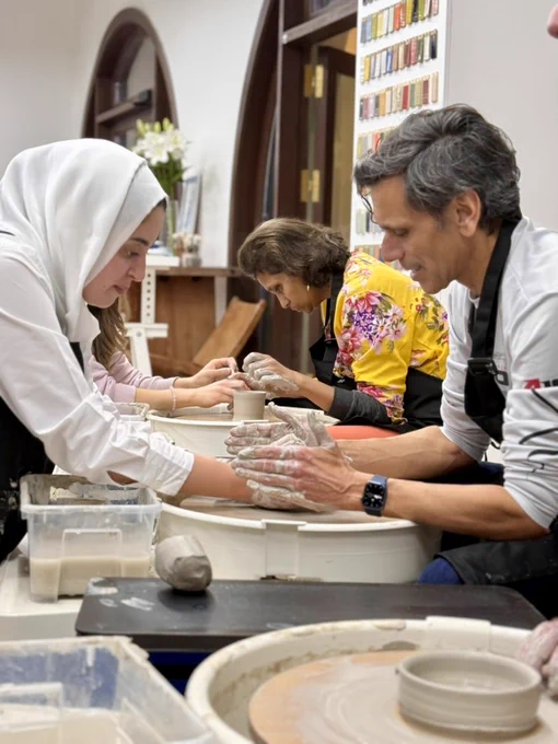 A woman helps Dr. Rao throw clay on a wheel.