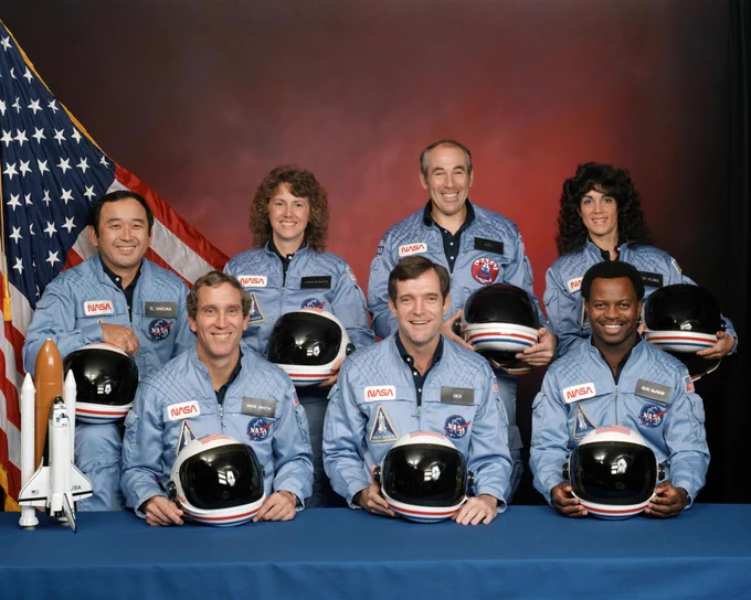 The STS-51L crew pose for a group portrait and smile in their light blue flght suits. From left to right: Mission Specialist Ellison S. Onizuka, Pilot Michael J. Smith, Payload Specialist Christa McAuliffe, Commander Francis R. \u201CDick\u201D Scobee, Payload Specialist Gregory B. Jarvis, Mission Specialist Judith A. Resnik, Mission Specialist Ronald E. McNair. Credit: NASA