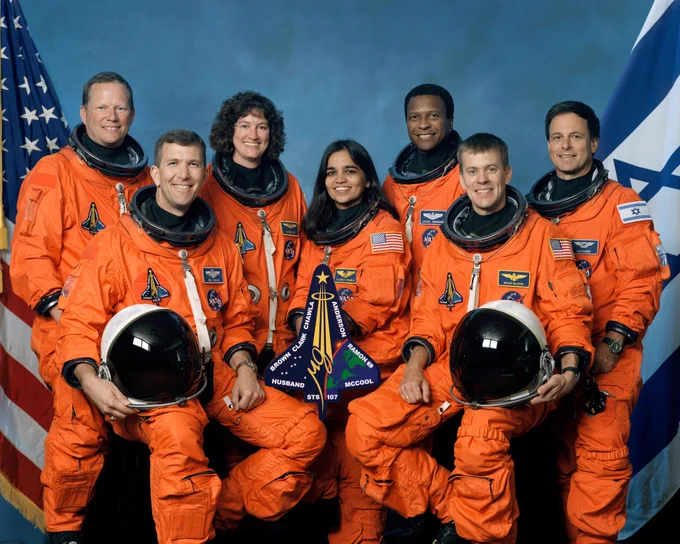 The STS-107 crew posing for a portrait in their orange spacesuits. Crew seated in front, from left, are: Astronauts Rick D. Husband, mission commander; Kalpana Chawla, mission specialist; and William C. McCool, pilot. Standing, from left, are: David M. Brown, Laurel B. Clark, and Michael P. Anderson, all mission specialists; and Ilan Ramon, payload specialist. Credit: NASA