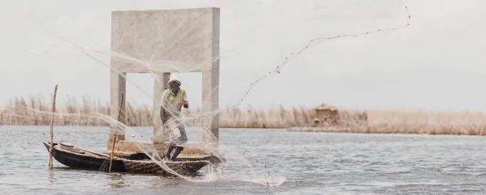 A man in a boat on a river casts a net into the water.