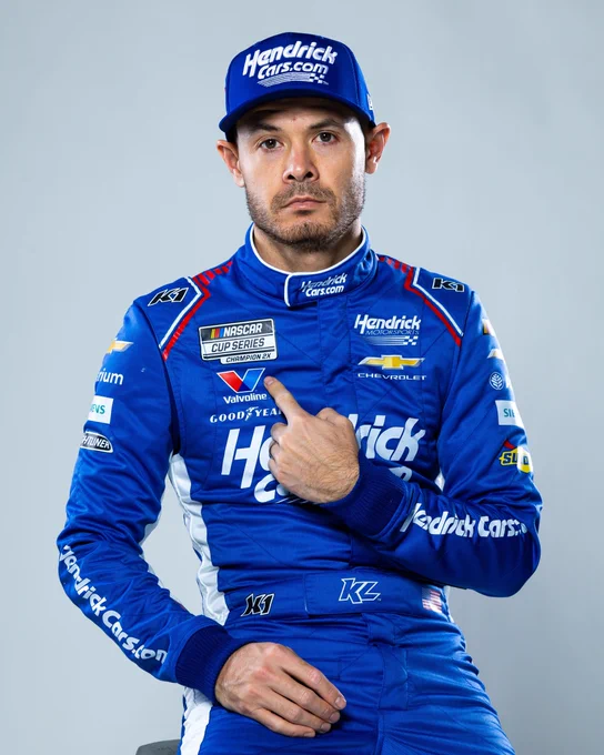 A photo of Kyle Larson pointing to his two-time champion patch on his fire suit. 