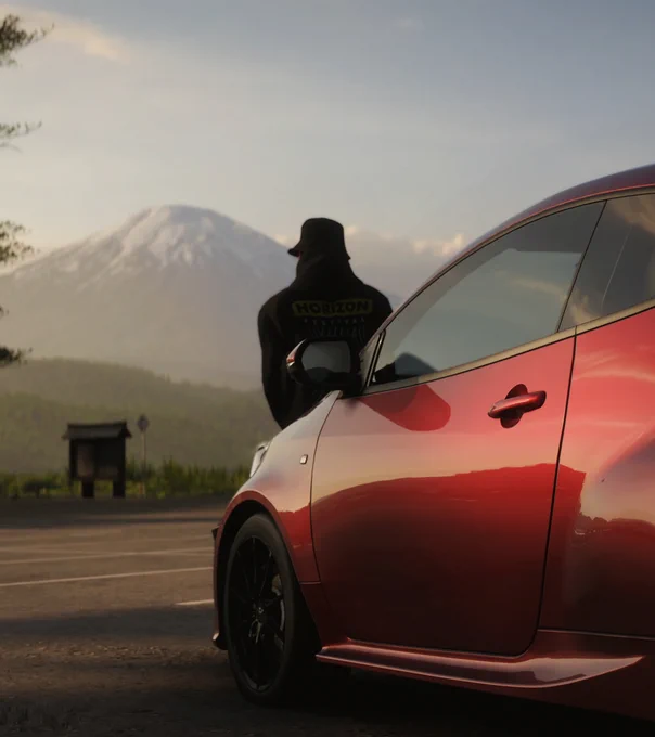 Screenshot from Forza Horizon 6 of a character leaned against the hood of a red car with Mt. Fuji in the background.