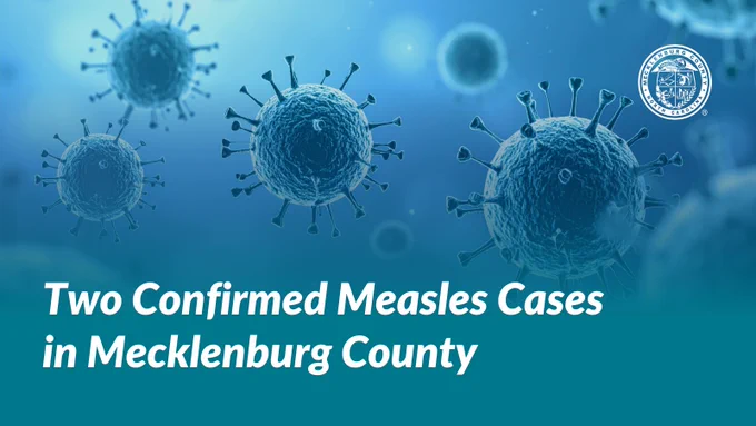 Graphic of two detailed measles viruses on a light blue background, with text stating 'Two Confirmed Measles Cases in Mecklenburg County' and the official seal of Mecklenburg County at the top.
