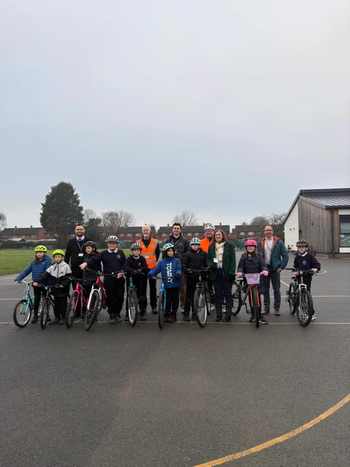 Group of children and adults standing with bicycles on a school playground under an overcast sky.