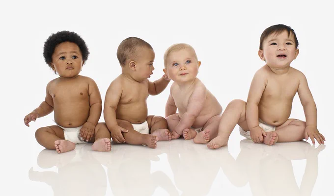 Four infants sitting side by side on a white background.