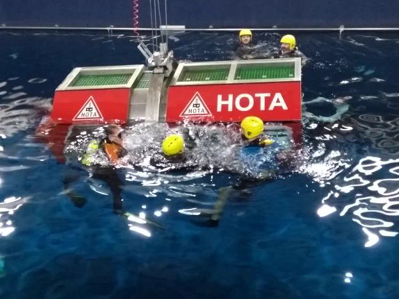 Several people in a large pool of water swimming next to a partly submerged vehicle
