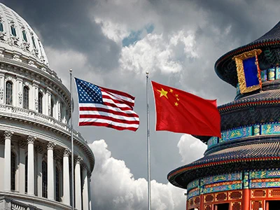 American and Chinese flags flying side by side against a cloudy sky, with the U.S. Capitol dome and traditional Chinese temple visible.