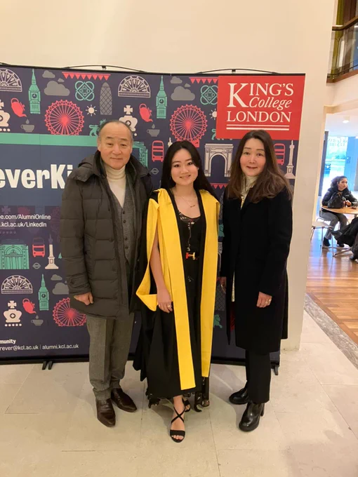 A graduate in a yellow and black graduation gown posing for a picture with their family in front of the ForeverKings sign.