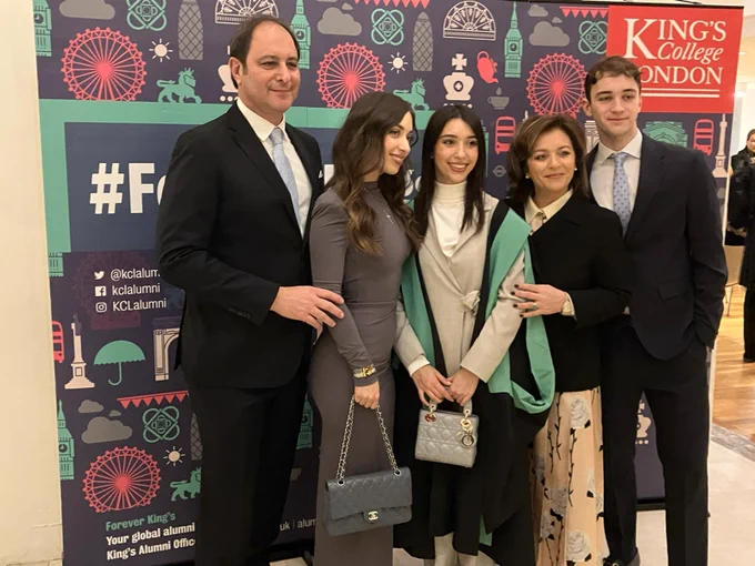 A graduate in a green and black gown posing for a picture with friends and family in front of the forever King's sign.