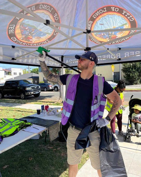 Person posing with trash picker in a tent with a "City of Long Beach" logo at a community clean up event.