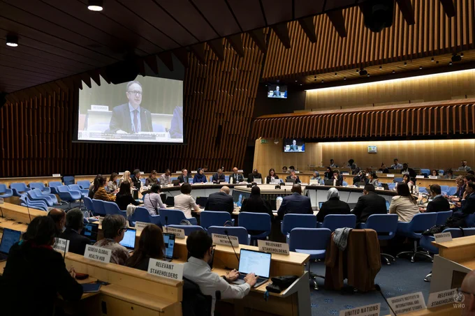 WHO Member States representatives seated in a large conference room with a speaker shown on a screen addressing the room.