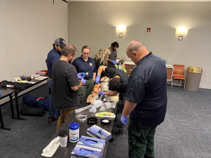 Personnel are in a training for the Operational Medical Support Program, learning how to administer care for other personnel while in the field. 