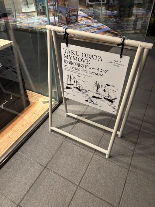 アニエスベーのガラス貼り店舗前に設置された展示の案内看板。白黒。
