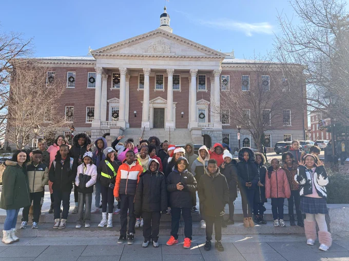 Group of diverse students posing in front of a historic building with columns on a clear day.