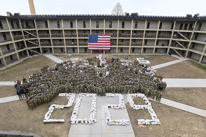 The VMI Class of 2029 - formerly the 2026 3 Rat Mass - poses for a group photo in barracks with sandbags they carried in to form the numbers 2 0 2 9. The American Flag and members of the Corps of Cadets can be seen in the background.